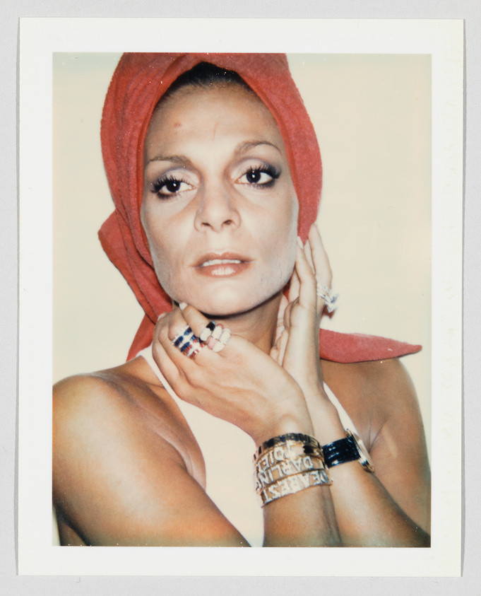 Person with a red towel wrapped around their head, wearing rings and bracelets, looking directly at the camera.