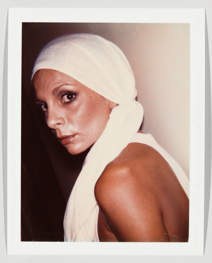 Person with a white headscarf looks over their shoulder, showing a serious expression and bare shoulder.