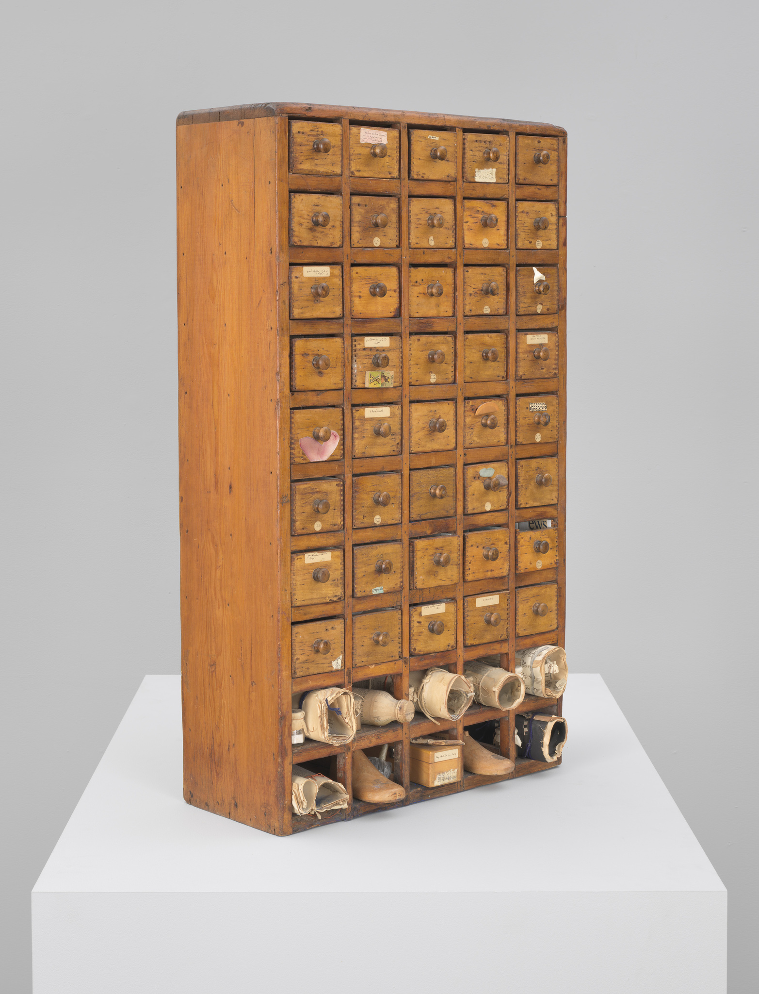 Vintage wooden cabinet with numerous small drawers, some labeled, and bottom shelves filled with rolled-up papers.