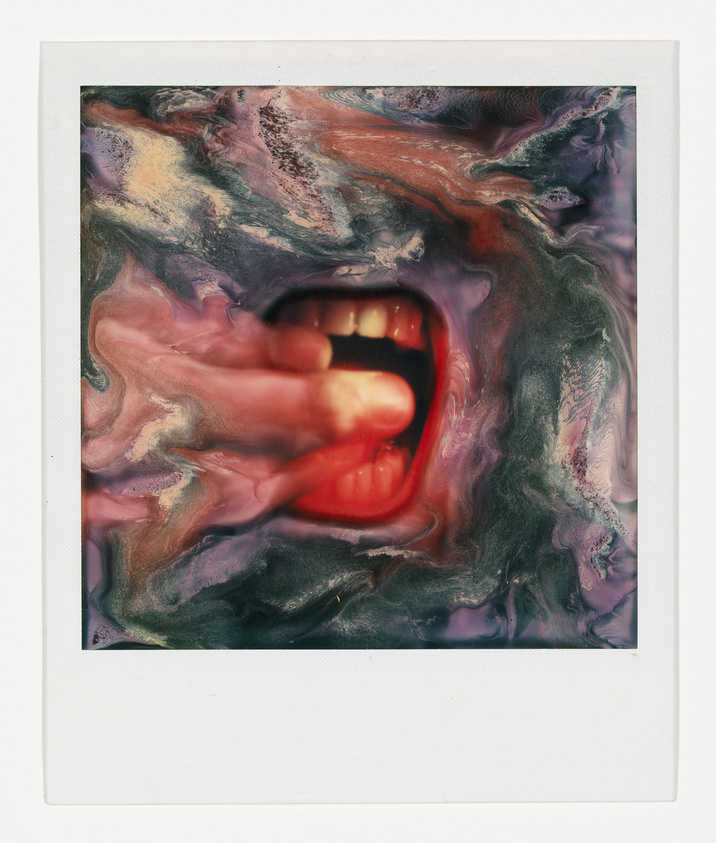 A Polaroid-style photograph depicting an abstract composition with swirling colors of red, purple, and black surrounding a central, clear image of a mouth with red lips and white teeth slightly parted. The overall effect is surreal and artistic, with the mouth appearing to emerge from the chaotic background.