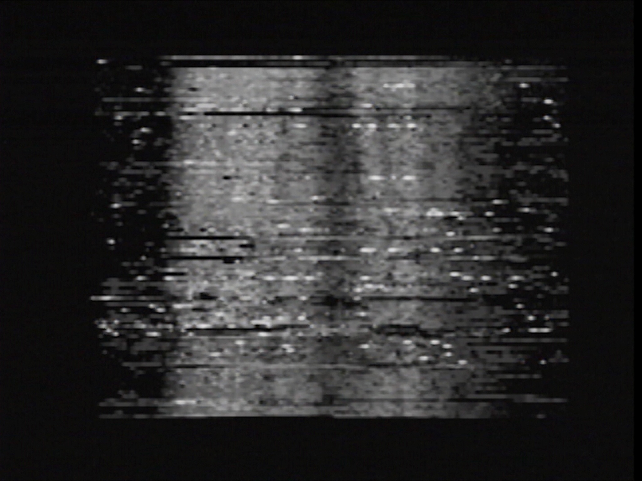 A heavily pixelated and glitched black and white image that appears to be a corrupted digital photo or video still, making it difficult to discern any clear details.