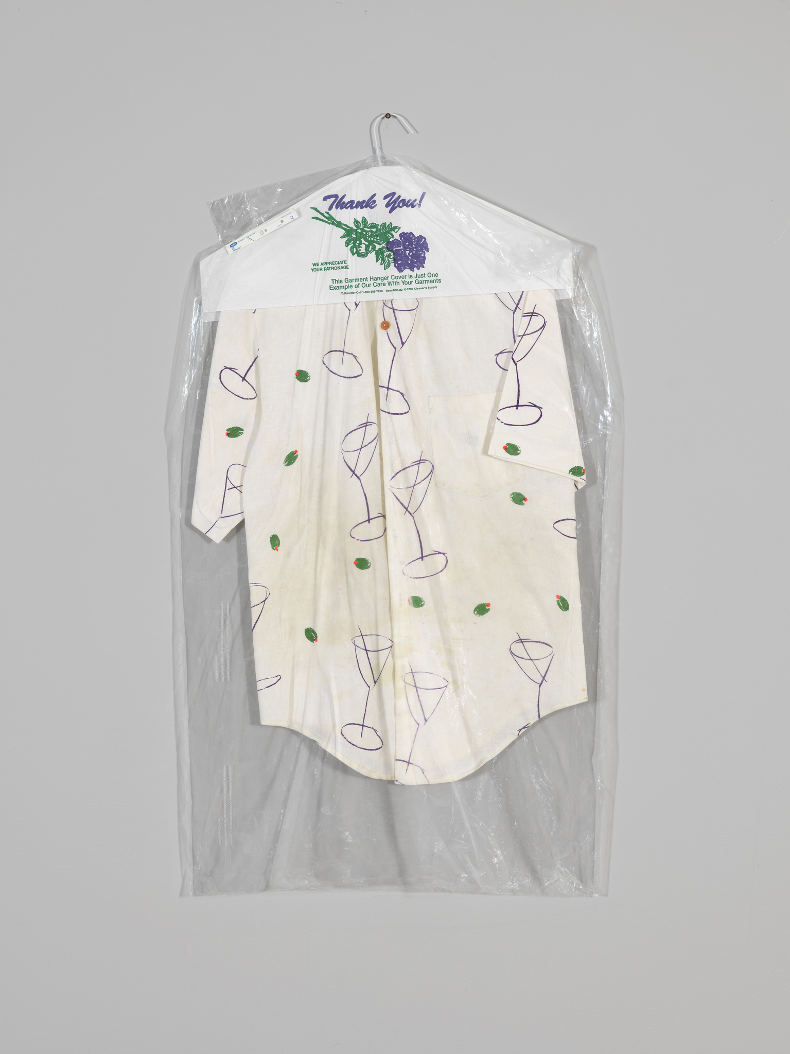 A white shirt with purple and green designs hangs on a hanger in a dry cleaner’s plastic cover.