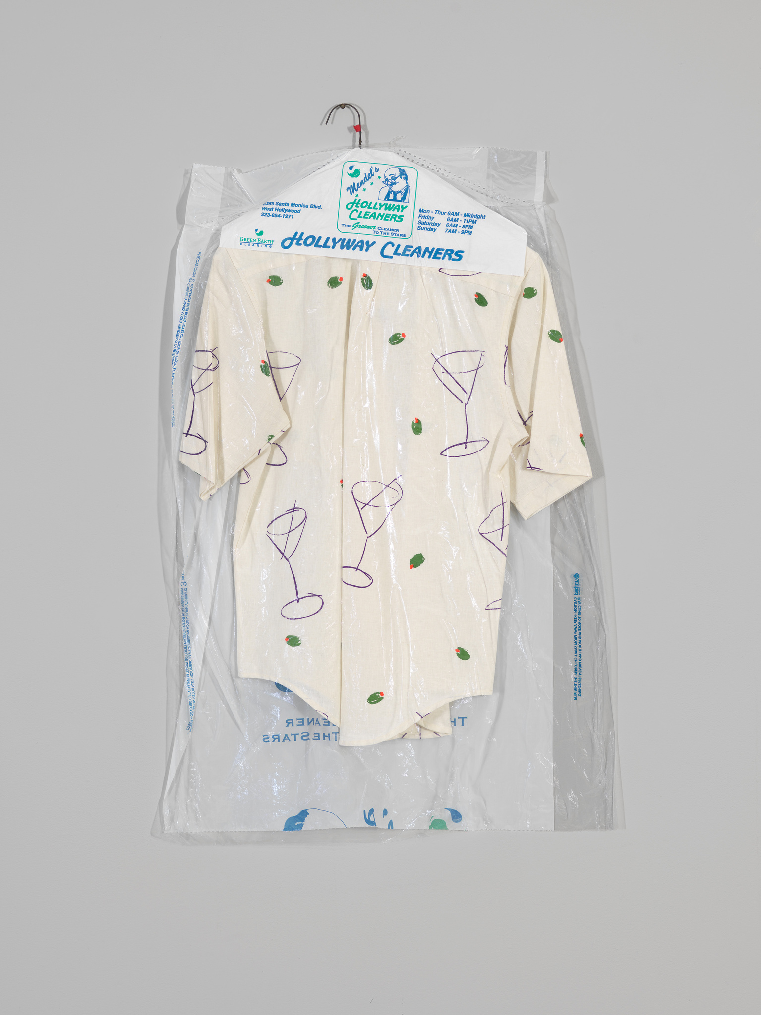 Short-sleeve shirt with martini glass and olive print, hanging in a clear dry cleaner bag labeled "Hollyway Cleaners."