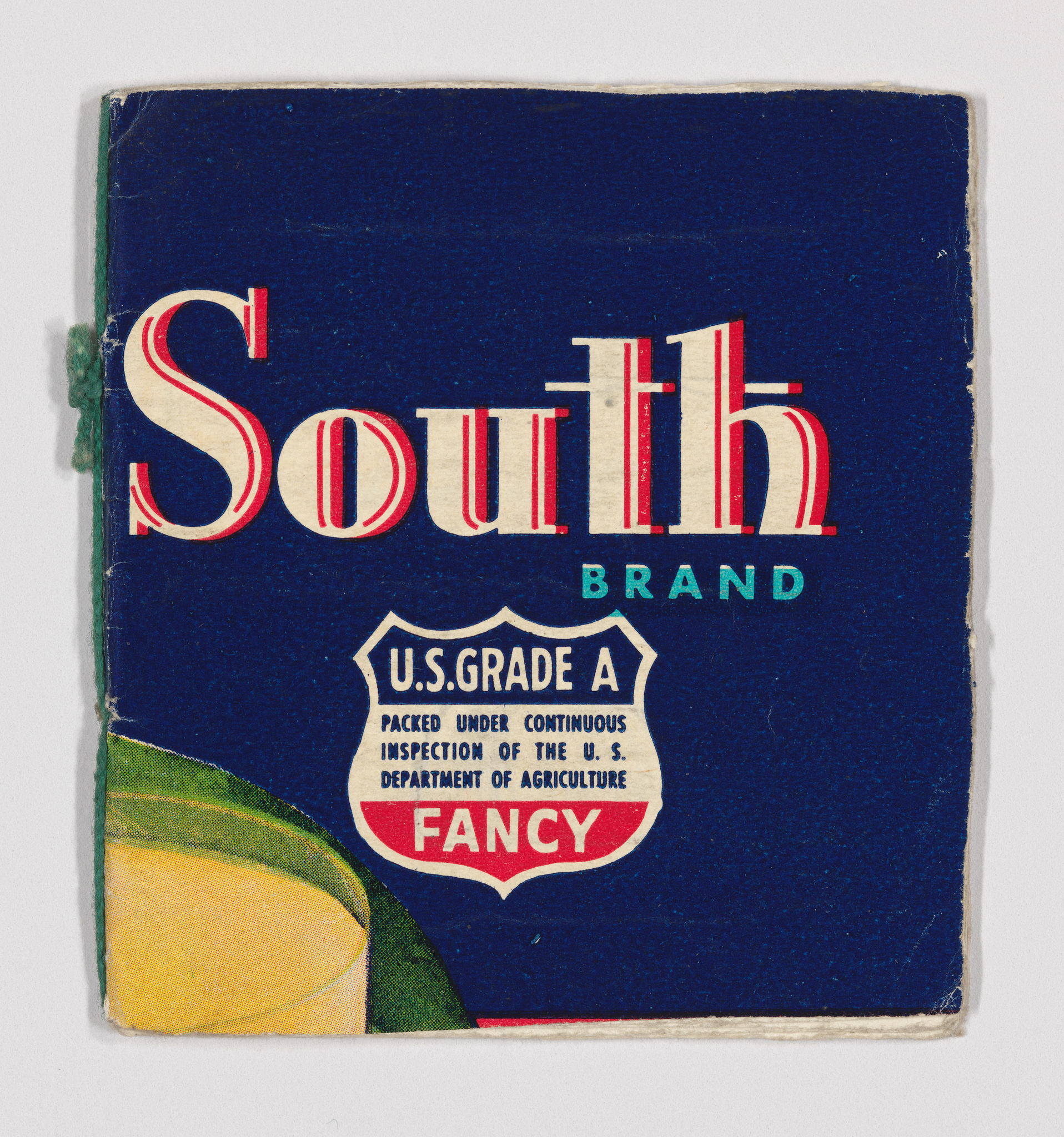 Vintage packaging for "South Brand" with a U.S. Grade A label, indicating it was packed under continuous inspection of the U.S. Department of Agriculture and marked as "FANCY." The packaging has a dark blue background with red and white text and a partial illustration of a yellow fruit with green leaves, possibly a lemon, in the bottom left corner. The edges of the packaging show signs of wear and age.