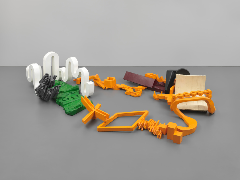 Abstract colorful sculpture resembling deconstructed furniture pieces on a grey floor.
