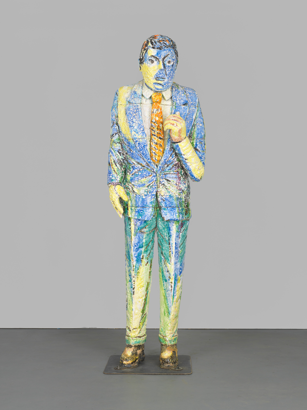 Colorful textured sculpture of a standing man in a suit with a tie, against a grey background.