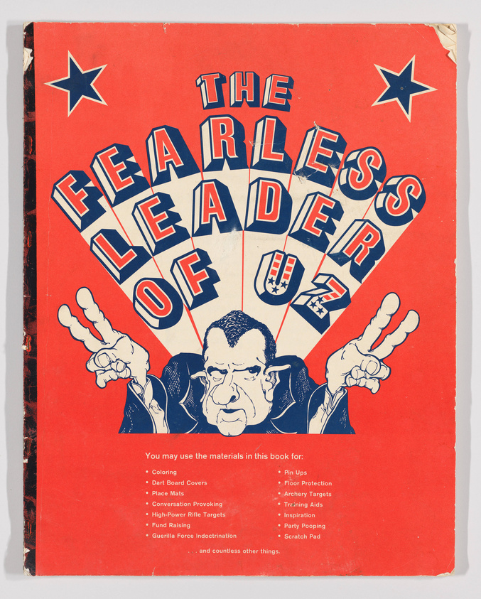 Vintage book cover with a bold red background featuring the title "The Fearless Leader of UZ" in large white and blue letters, with a caricature of a man's face in the center. The caricature is surrounded by blue rays emanating from behind his head, creating a dramatic effect. Below the title and image, a list of suggested uses for the book's materials includes coloring, dart board covers, place mats, and more, with a humorous tone suggesting unconventional uses such as "Guerrilla Force Indoctrination" and "Party Pooping." The cover shows signs of wear and tear, indicating its age.