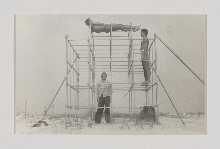 Three people on a metal structure at the beach, one lying on top, two standing below.