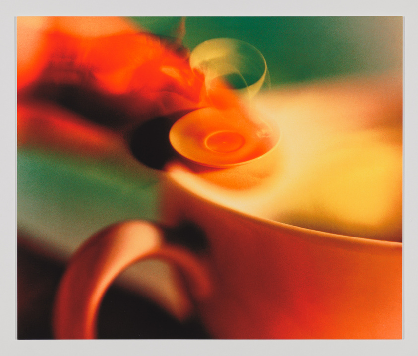 A close-up, abstract and blurred image of a steaming cup of coffee or tea, with warm colors and a soft focus that creates a dreamy atmosphere.