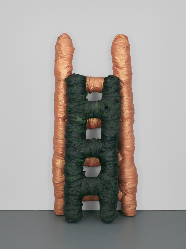 Sculpture resembling a letter 'H' with textured, peach-colored sides and a green, wrinkled center against a grey background.