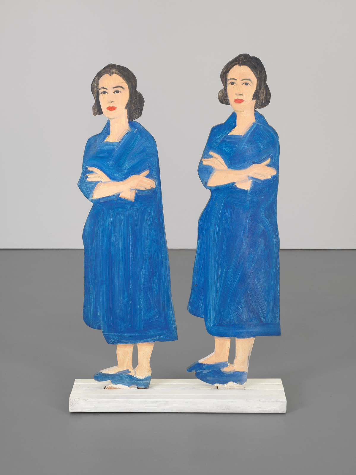 Two wooden cutout figures of a woman in a blue dress, standing back-to-back on a white base.
