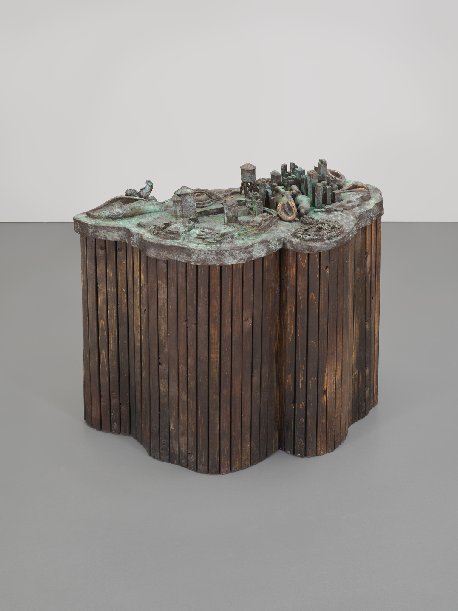 Sculpture with a wooden base and a top surface showing a small cityscape with buildings and a water tower.
