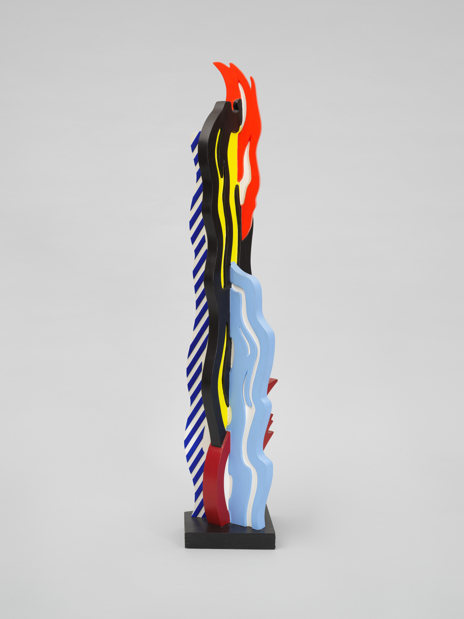 A colorful abstract sculpture with wavy layers of red, yellow, blue, and black stripes against a plain light background.