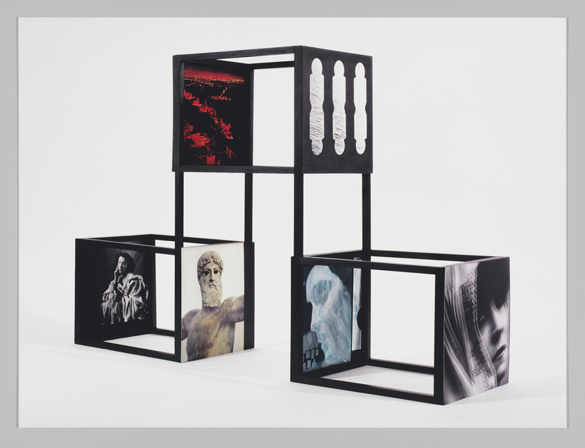 A modern art installation featuring a series of black cubic frames arranged in a geometric sculpture. Each cube contains a different monochromatic image, including a red-toned cityscape, a classical painting, a sculpture of a bearded man, a blue-tinted portrait, and a photograph of a woman's face partially obscured by shadow or fabric. The overall composition is set against a white background, creating a stark contrast.