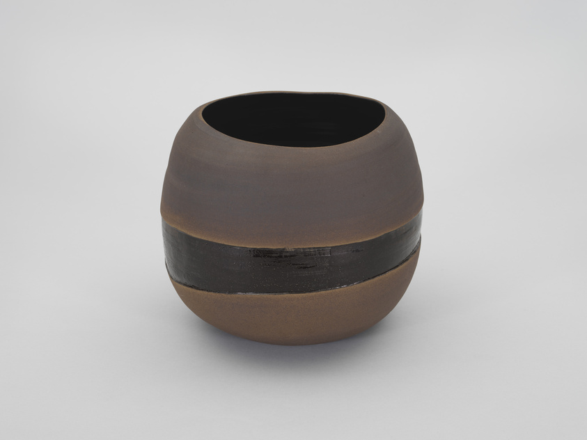 A ceramic bowl with a smooth, rounded shape and a matte finish. The bowl features a natural brown color with a distinctive black horizontal band around its midsection. The interior of the bowl appears to be glazed in black. It is photographed against a plain, light background.
