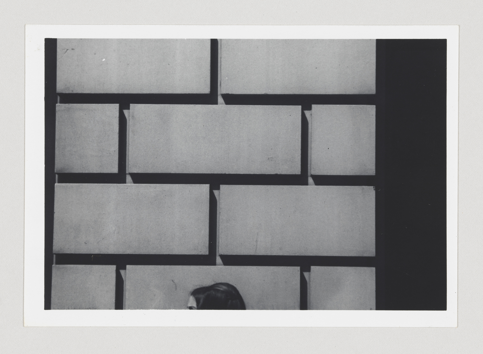 A black and white photograph showing a pattern of rectangular blocks with a person's head partially visible at the bottom edge, creating an abstract composition.