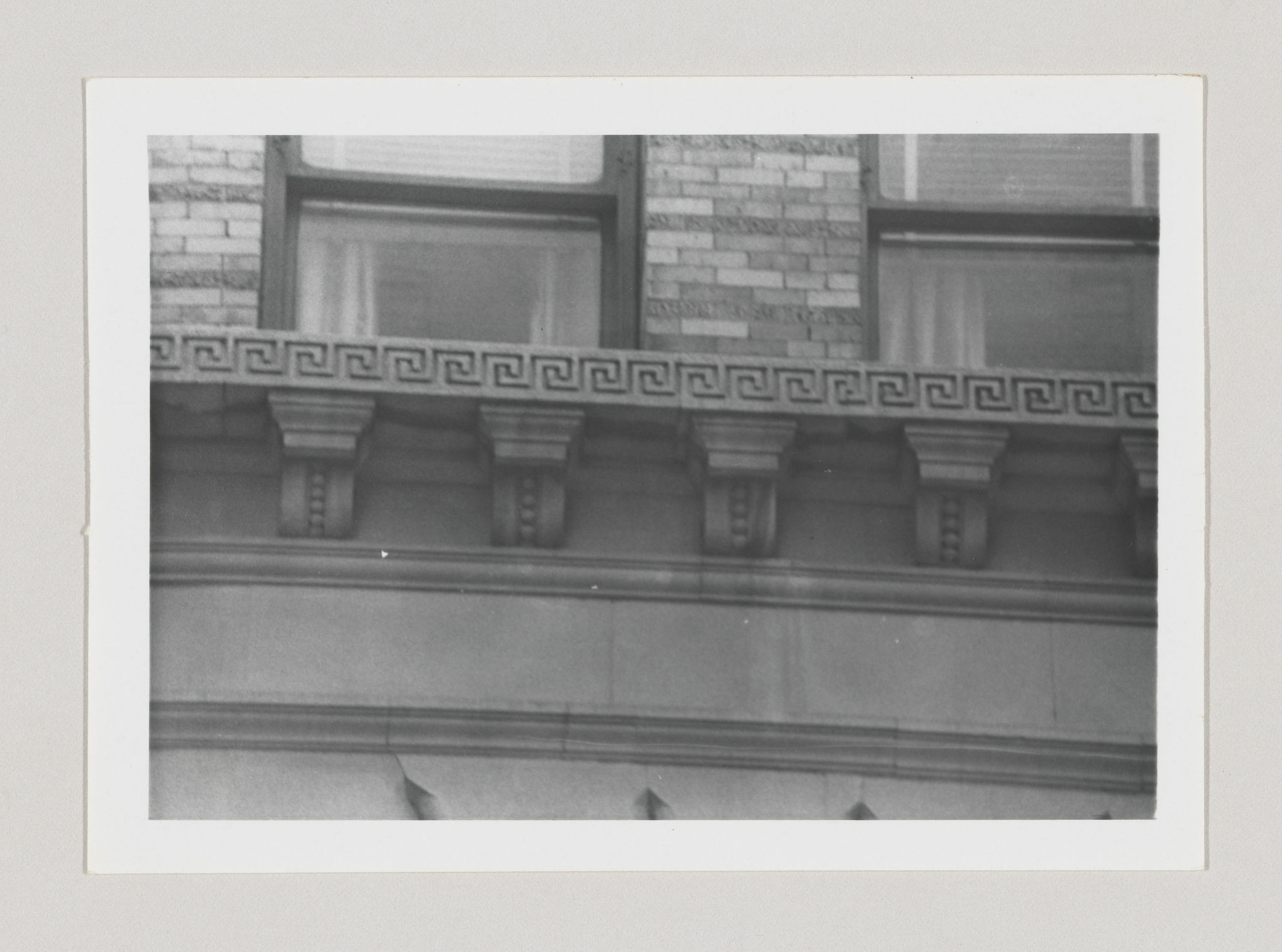 A black and white photo of the architectural details on the facade of a building, showing a row of windows with decorative molding and a Greek key pattern just above them.