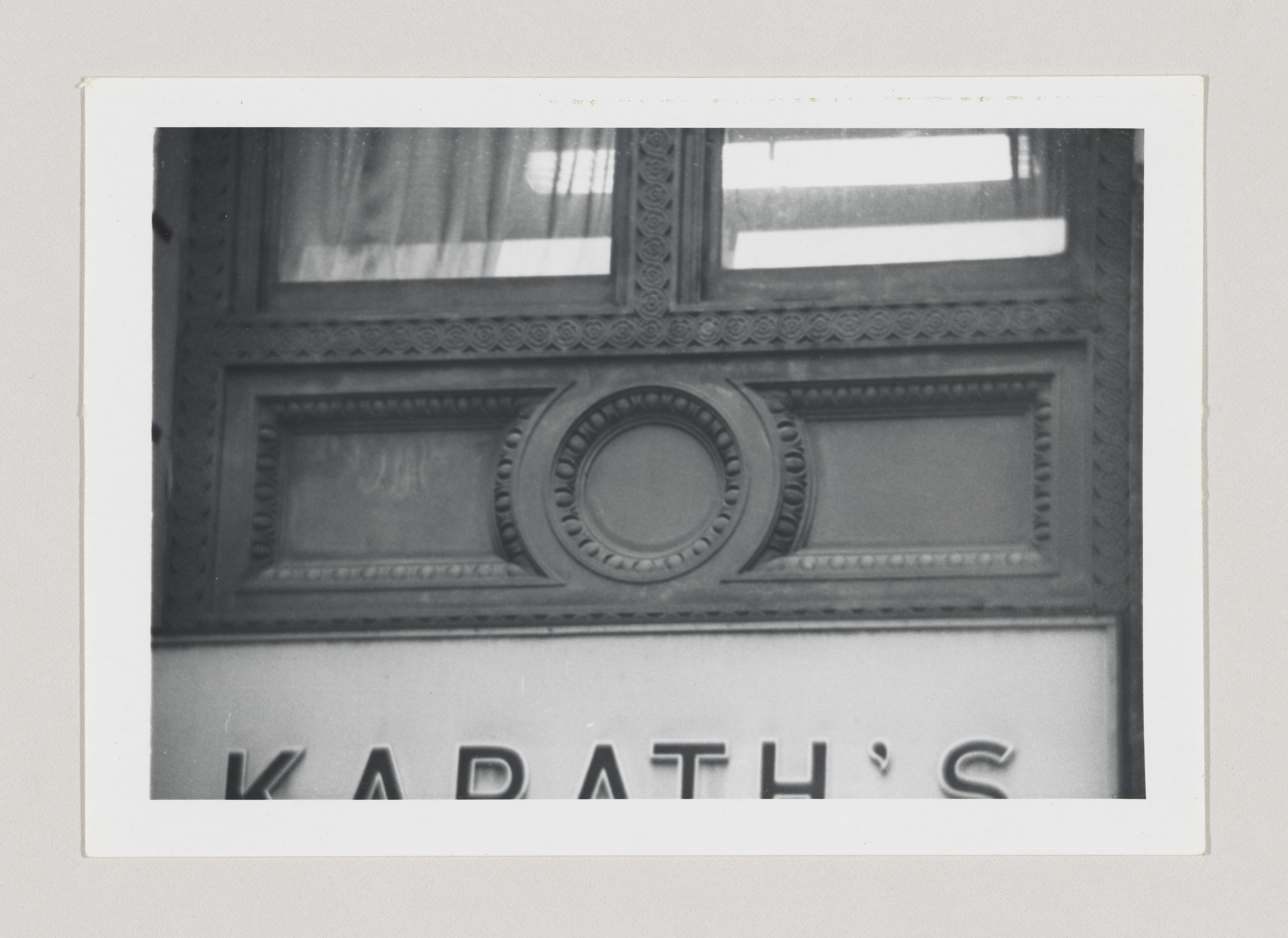 Black and white photo of an ornate building detail with a circular design and the word "KARATH'S" in capital letters visible at the bottom.