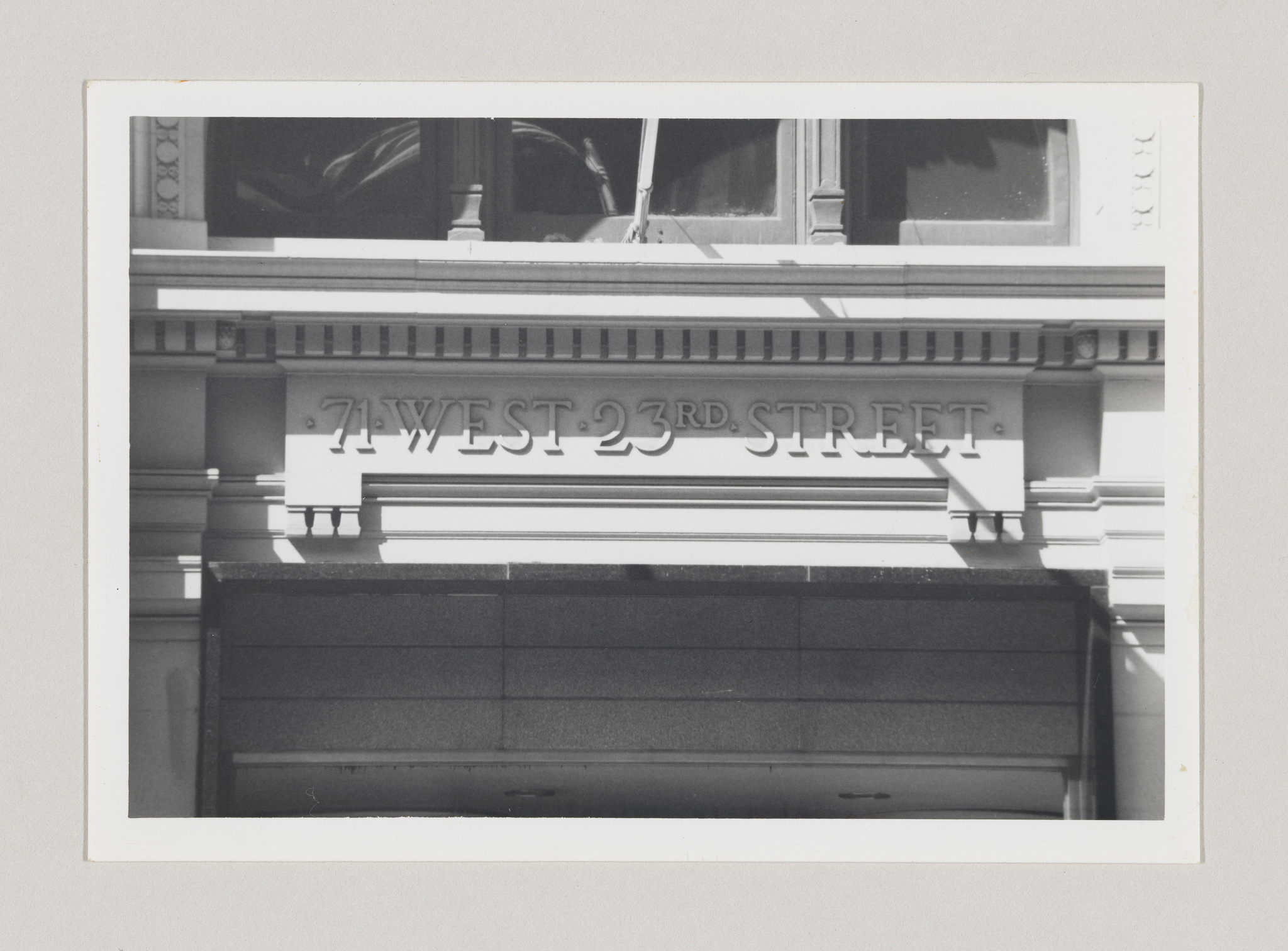 Black and white photo of a building facade with the address "71 West 23rd Street" prominently displayed in raised lettering above a stone ledge.
