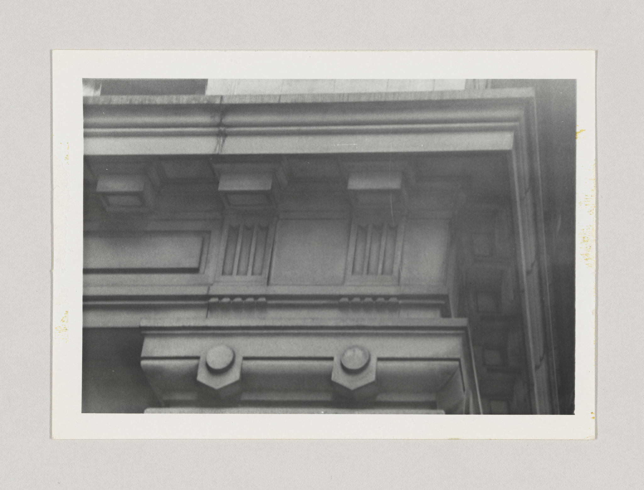 A black and white photograph of architectural details showing the cornice and frieze of a classical building with decorative molding and dentils. The photo has a white border and shows signs of age with slight discoloration on the edges.