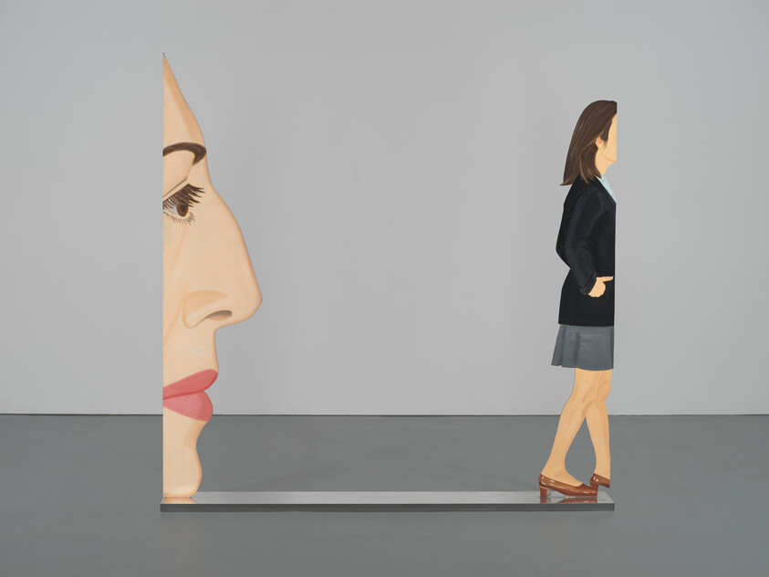 Sculpture of a woman’s face in profile connected to a walking woman, both painted in a simple style.