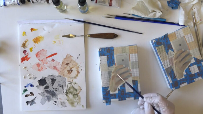 Artist painting a hand holding a phone on two canvases, surrounded by brushes, a palette with paint, and art supplies on a table.