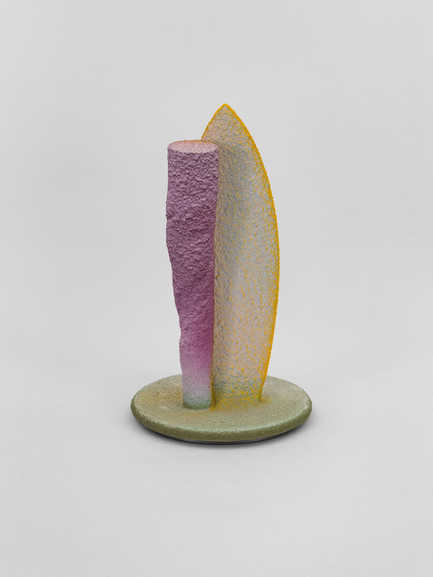 A textured sculpture featuring a cylindrical purple form and a curved yellow form standing upright on a green circular base against a white background.