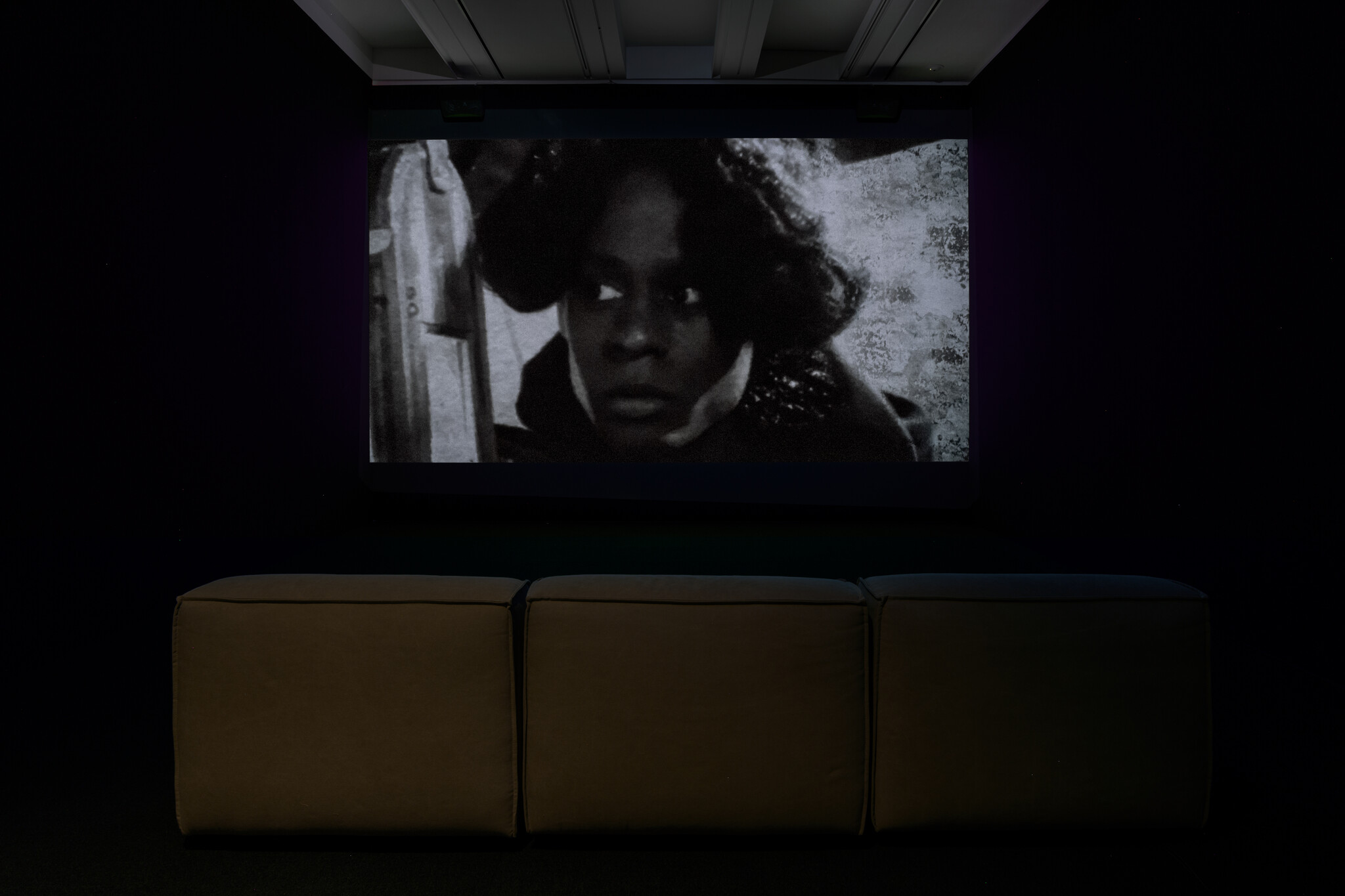 A black-and-white film is projected on a screen in a dark room with three seats.