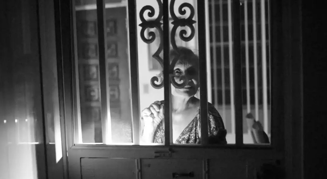 Woman peering through a window with ornate bars, black and white photo.