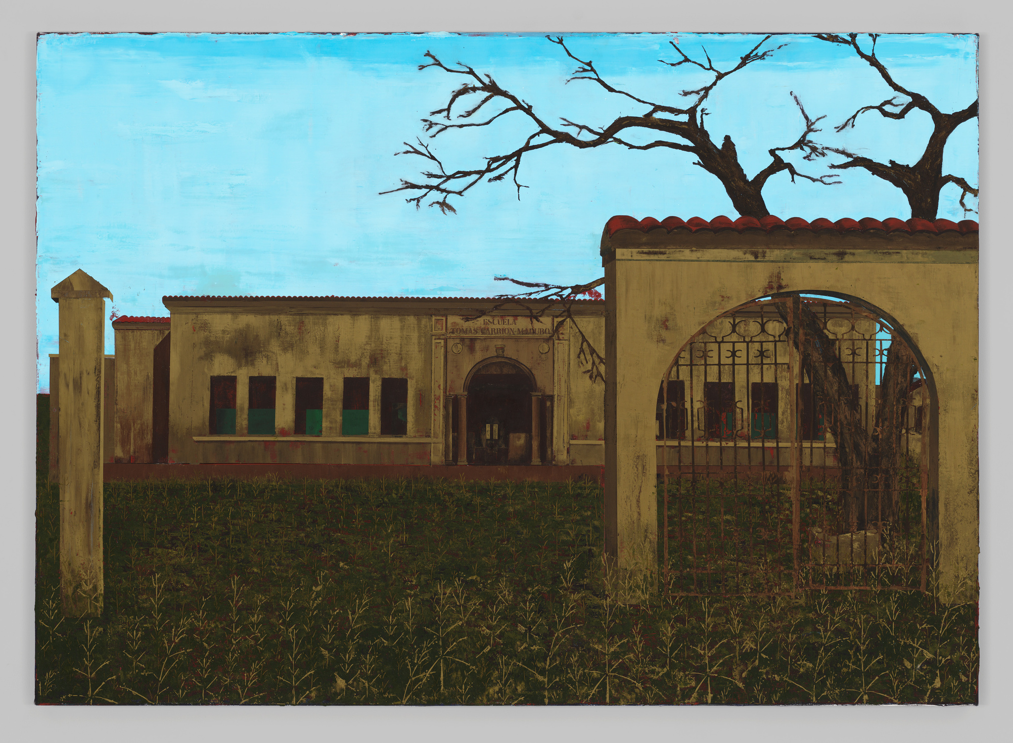 Old building with arched entrance, surrounded by overgrown grass and bare trees under a clear sky.