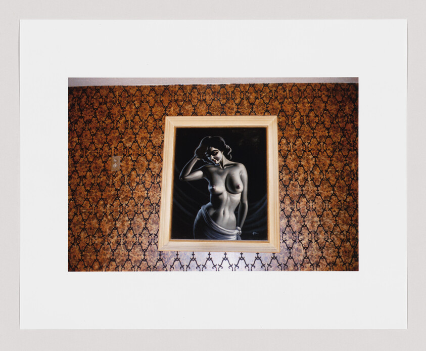 A framed painting of a topless woman hangs on a patterned brown wallpapered wall.