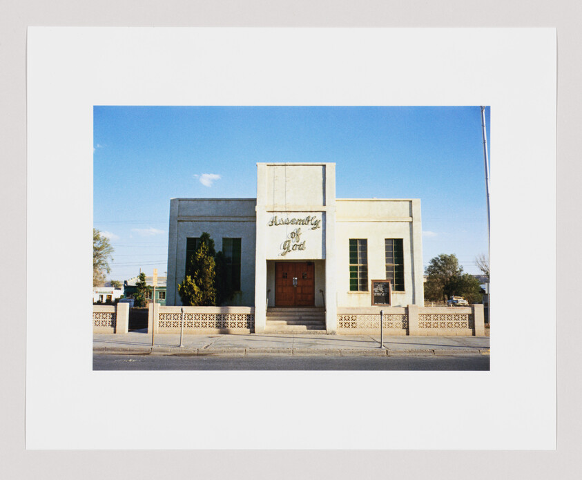 A beige church building with green windows and a sign above the door that reads "Assembly of God."