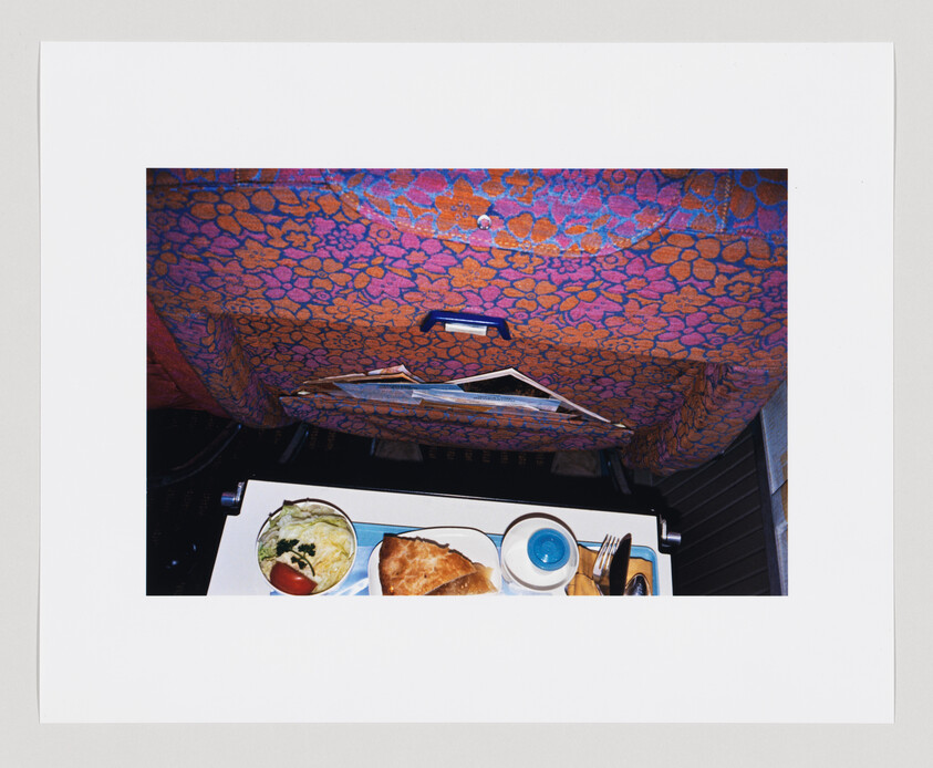 Airplane seatback with a tray table holding a meal, including salad, bread, and a cup.