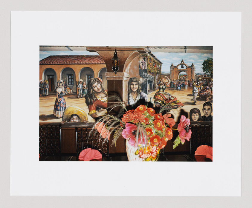 A vase with bright pink and orange flowers sits in front of a colorful mural showing people at a festival.