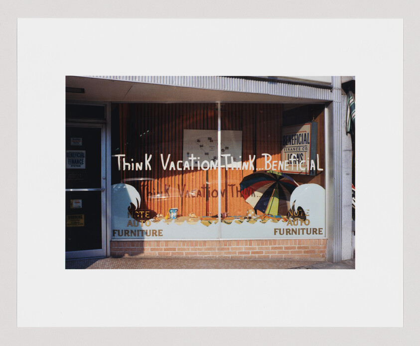 Storefront window with the words "Think Vacation Think Beneficial" and a large umbrella displayed inside.