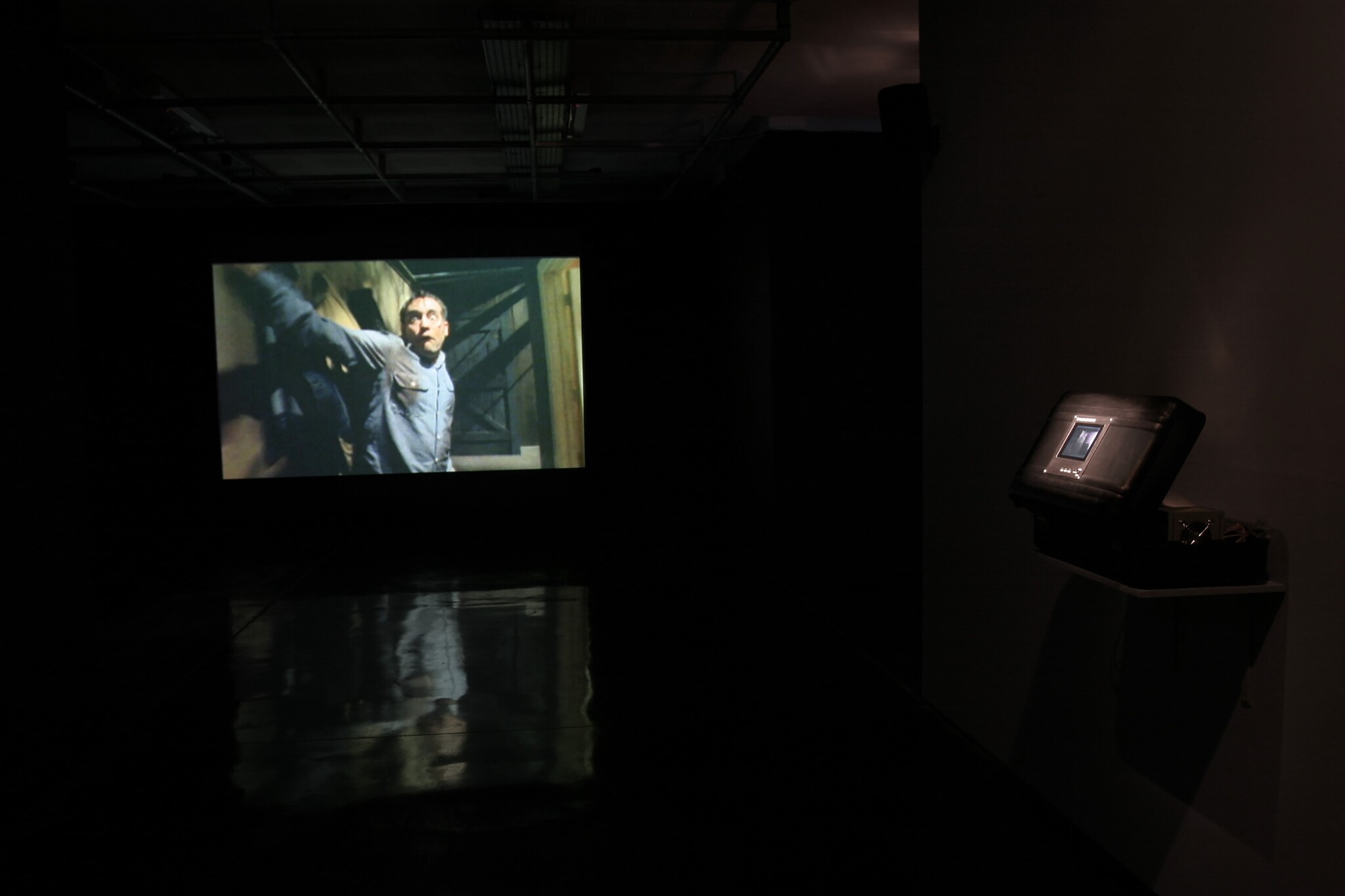 A man in a blue shirt is projected on a screen in a dark room.
