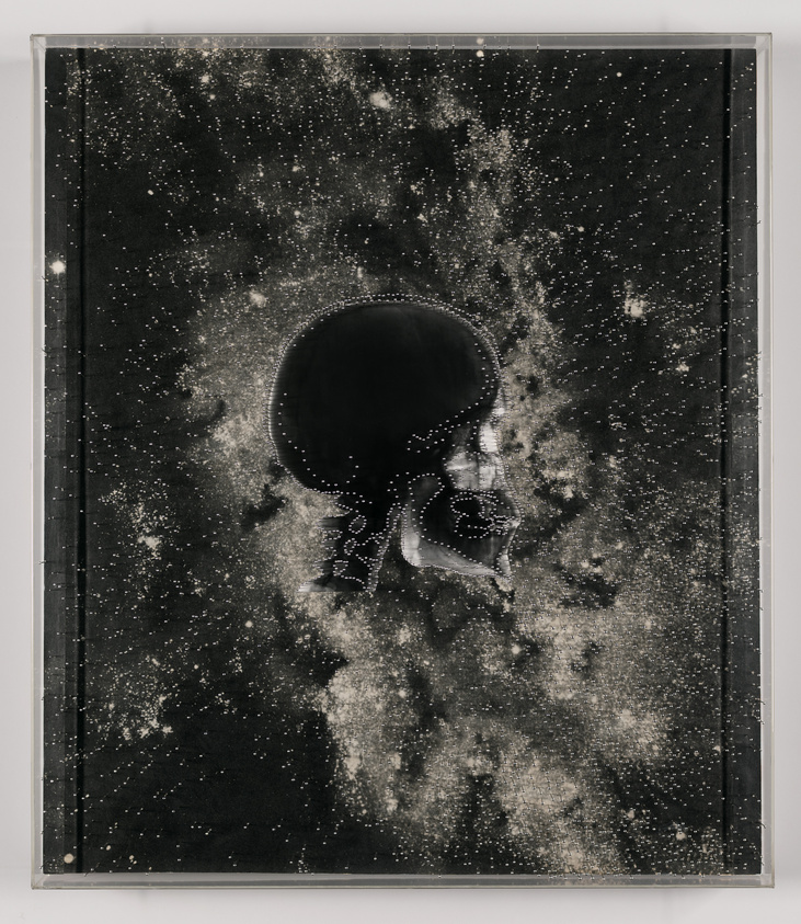 A framed artwork depicting a cosmic scene with a large, dark, skull-like shape at the center surrounded by a field of white speckles resembling stars against a black background. The skull shape is detailed with white outlines that give it a nebulous, ethereal appearance.