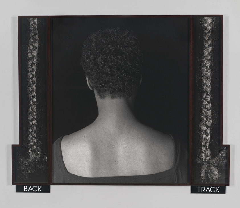 The head and shoulders of a short-haired Black woman in a dark blouse with her back to the camera. Single strands of dark braided hair hang on either side of her above text that reads "BACK" and "TRACK"