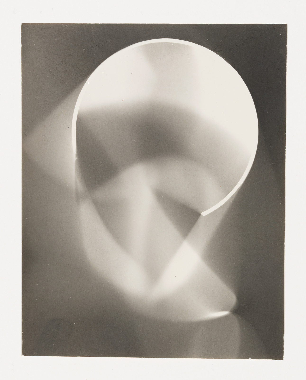 A black and white photograph featuring an abstract composition with a prominent curved shape creating a sense of depth through light and shadow. The image captures the interplay between geometric forms and the gradations of light, resulting in a minimalist yet evocative visual experience.