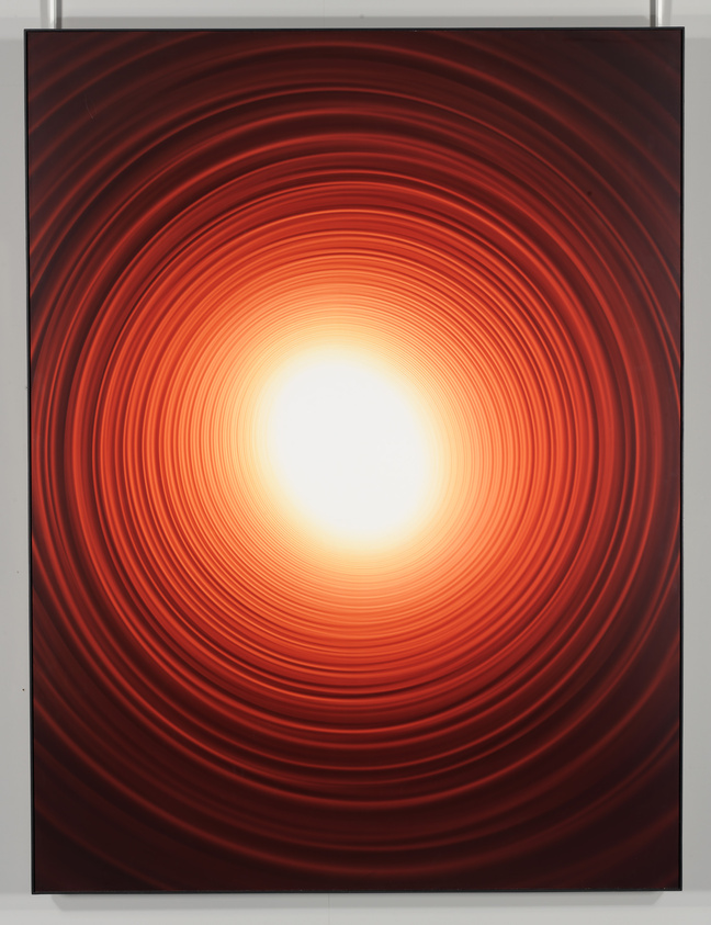 A vibrant artwork featuring concentric red and orange circles radiating from a bright white center, creating a tunnel-like effect.
