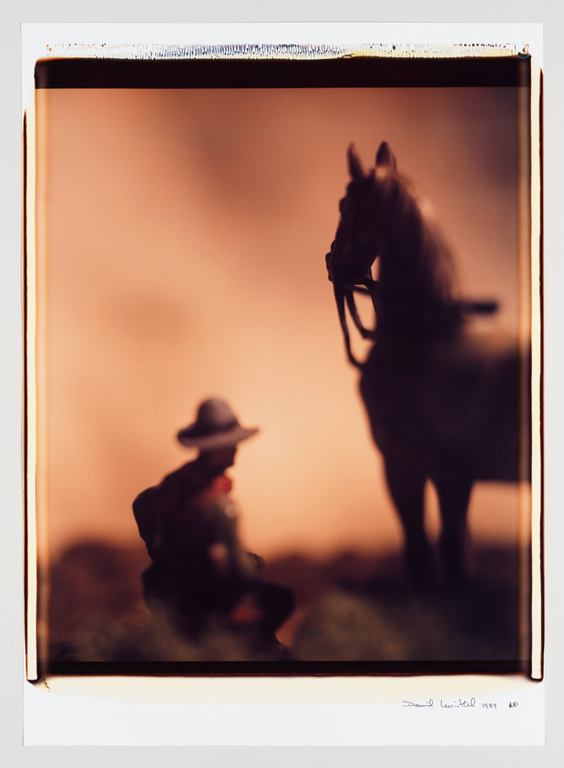 A silhouette of a cowboy holding the reins of a horse against a warm, gradient background, captured within the borders of a Polaroid frame. The image has a signature and date on the bottom right.