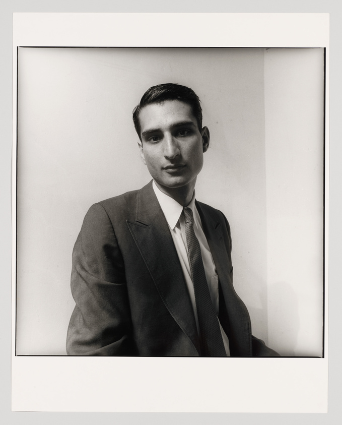Black and white portrait of a young man in a suit and tie, looking directly at the camera with a neutral expression, framed against a plain background.