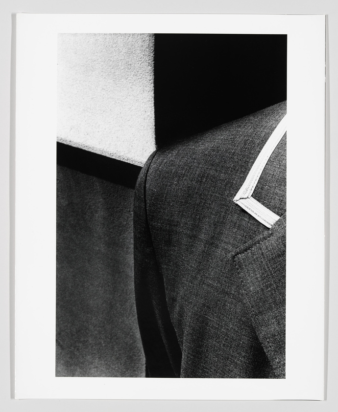 Black and white photograph focusing on the texture and contrast of a piece of fabric, possibly clothing, with a distinct white tag or label attached to it. The image is framed with a white border.