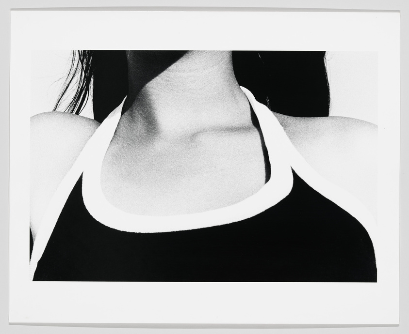A high-contrast black and white photograph focusing on the neck and shoulders of a person wearing a dark tank top with a prominent white trim. The person's face is not visible, and the background is completely white.