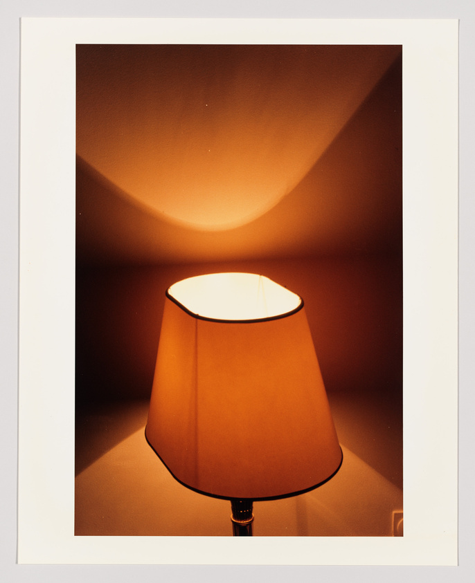 A warmly lit table lamp with an orange shade casts a soft glow on a plain wall, creating a cozy atmosphere.