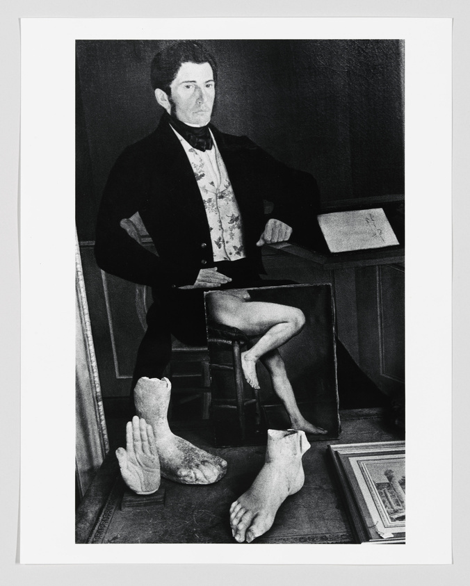 Black and white photograph of a painting depicting a seated man in 19th-century attire with a book on a table beside him. In the foreground, there are two plaster casts of human feet and a hand, creating a surreal juxtaposition with the painted figure.