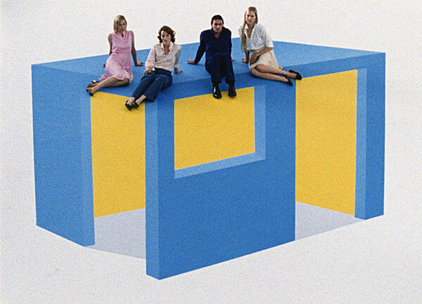 Three women and a man sit on a blue and yellow box.