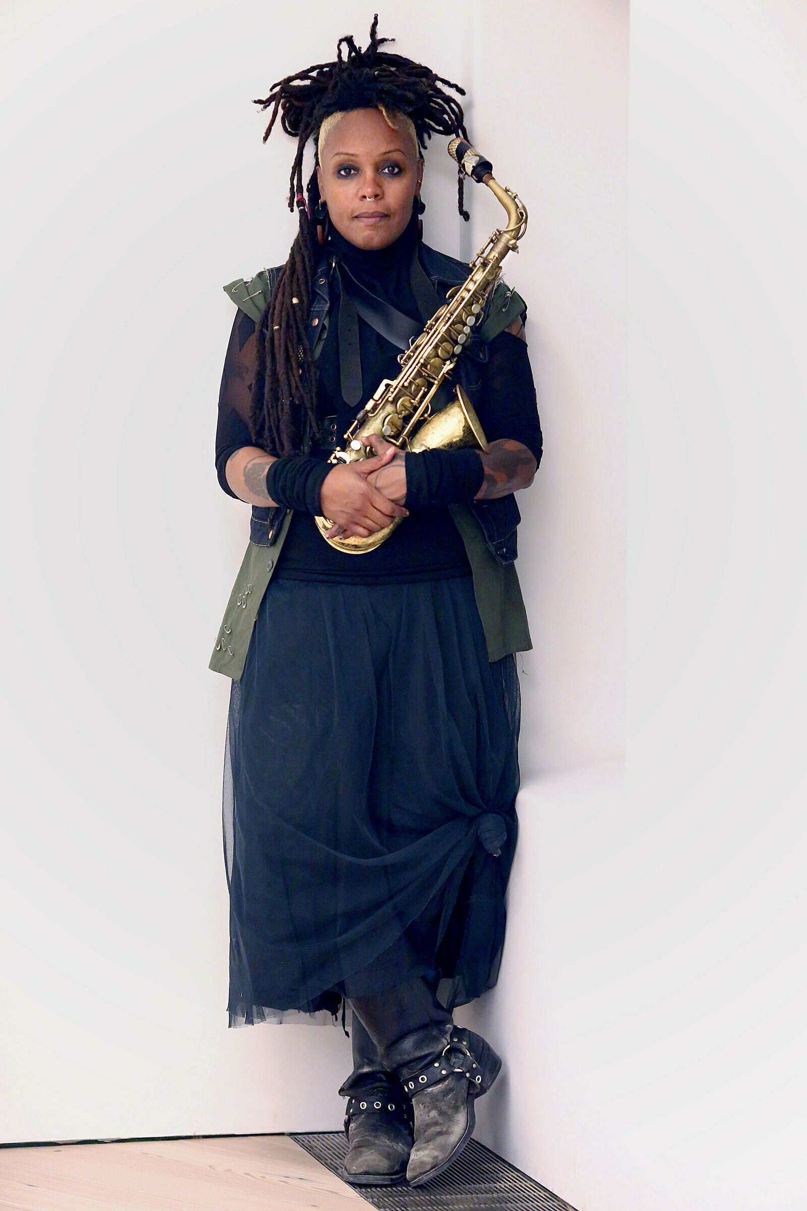 Matana Roberts leans against a wall with a saxophone.
