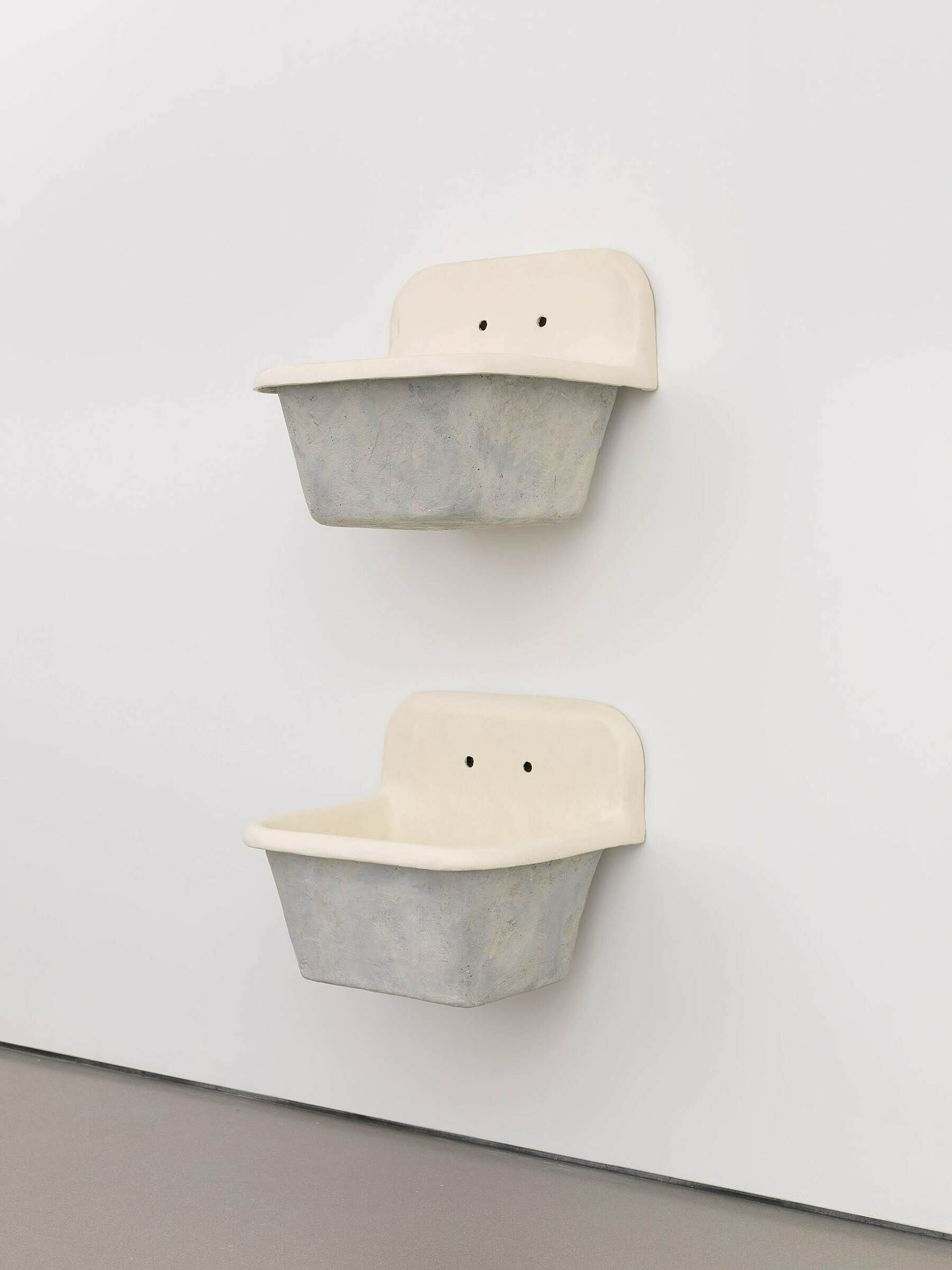 Two sculptures of sink basins attached to a wall.