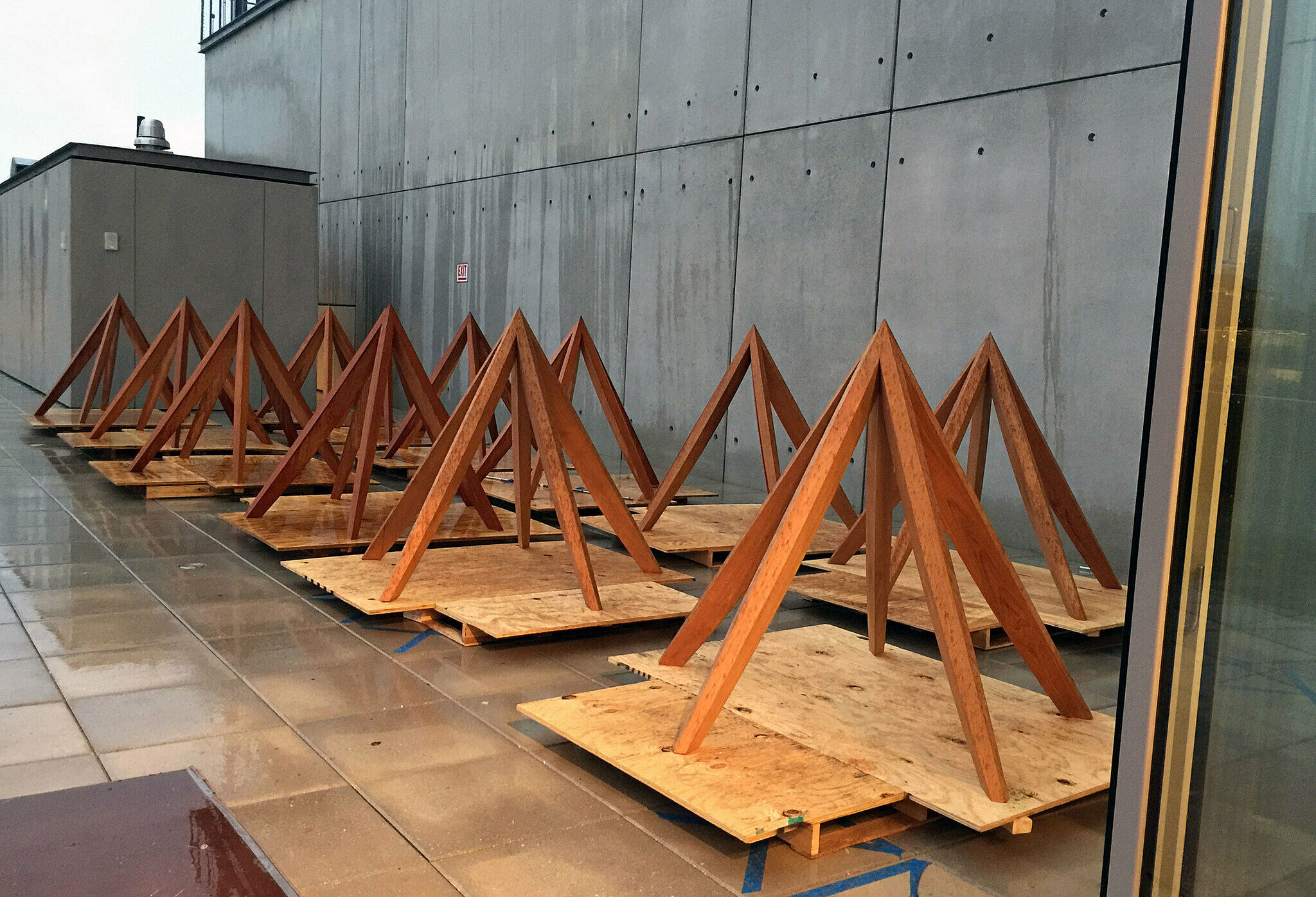 Wooden triangular structures on plywood bases are lined up against a concrete wall on a wet tiled floor.